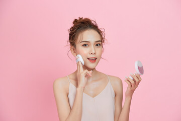 Wall Mural - Portrait of beautiful asian woman applying powder puff at cheek makeup of cosmetic isolated over pink background.