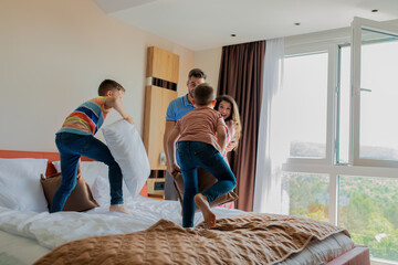 Wall Mural - family of four enjoying together at hotel room kids having fun playing with pillows.
