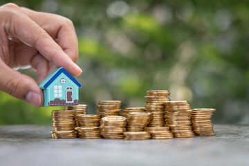 Money Financial, Business Growth,loan and real estate investment concept. Man hand put house model on gold coins to stack of coins.