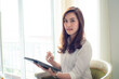 © themorningglory - Happy asian businesswoman using digital tablet sitting on sofa in bedroom over curtain background