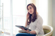 © themorningglory - Happy asian businesswoman using digital tablet sitting on sofa in bedroom over curtain background