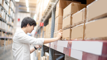 Wall Mural - Young Asian shopper man picking cardboard box package from product shelf in warehouse. Male customer shopping lifestyle in department store. Buying or purchasing factory goods. Inventory stock concept