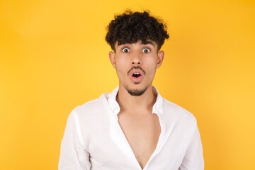 Emotional attractive male with opened mouth expresses great surprisment and frighteness, poses against white concrete background, stares at camera. Unexpected shocking news and human reaction.