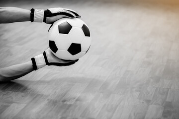 Sticker - Black and white image of ball in hands of futsal goalkeeper on wooden futsal floor. Indoor soccer sports hall. Football futsal player, ball, Sports background. Youth futsal league.