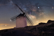 Low Angle Of Spectacular Landscape Of Rocky Mountain With Traditional Windmill On Background Of Amazing Milky Way In Dark Sky