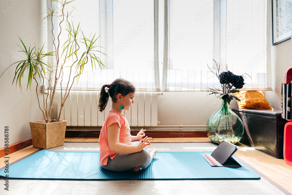 Full body little girl sitting in lotus pose and meditating on mat at ...