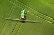 Tractor spraying chemical pesticides with sprayer on the large green agricultural field at spring.