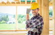 Smiling worker on building site with frame house construction in background