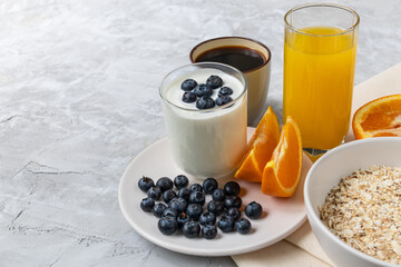 breakfast with yogurt with blueberry and juice, orange, oatmeal and coffee on concrete background