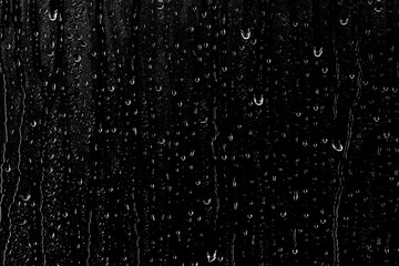 Drops of water flow down the surface of the clear glass on a black background. Texture for creativity.