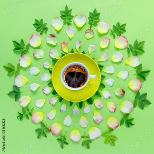 Beautiful floral pattern of pink rose petals and yellow cup of hot aromatic coffee on paper green background.