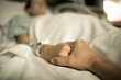 © kieferpix - Person giving sick loved one support. Man holding woman's hand lying in hospital bed.