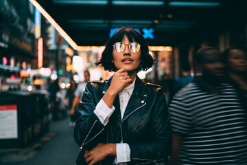 Youthful female traveller in stylish spectacles for vision correction spending time for walking around metropolitan downtown and explore New York nightlife on leisure, young woman in streetwear