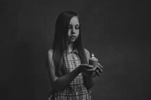 The Girl Stands With A Candle On A Dark Background. Black White Photo