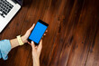 © Rymden - Mockup image of a woman using smartphone with blank screen on wooden table. Close up photo of female hands holding mobile phone vertically
