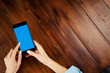 © Rymden - Mockup image of a woman using smartphone with blank screen on wooden table. Close up photo of female hands holding mobile phone vertically