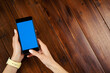© Rymden - Mockup image of a woman using smartphone with blank screen on wooden table. Close up photo of female hands holding mobile phone vertically