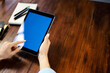 © Rymden - Mockup image of a woman using digital tablet with blank screen on wooden table. Close up photo of female hands holding device vertically