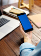 © Rymden - Mockup image of a woman using smartphone with blank screen on wooden table.