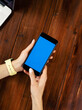 © Rymden - Mockup image of a woman using smartphone with blank screen on wooden table. Close up photo of female hands holding mobile phone vertically