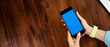 © Rymden - Mockup image of a woman using smartphone with blank screen on wooden table. Close up photo of female hands holding mobile phone vertically