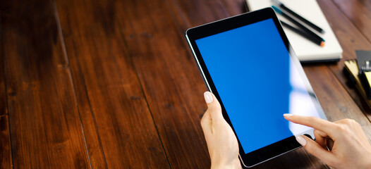 Mockup image of a woman using digital tablet with blank screen on wooden table. Close up photo of female hands holding device vertically