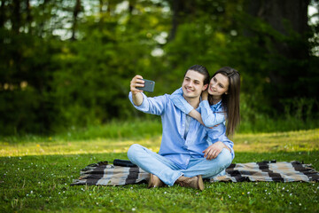 Sticker - Lovely couple have fun together, sit on plaid outdoor, enjoy sunny warm weather, pose for making selfie at camera