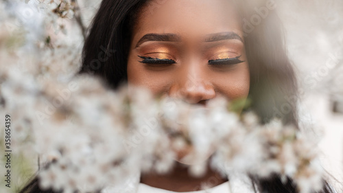 Fotografía Close-up face of a beautiful happy african black woman with closed eyes in flowers on a spring blooming day