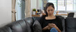 © bongkarn - A woman lying relaxed on couch in living room and texting message on smartphone