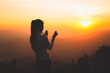A women is praying to God on the mountain. Praying hands with faith in religion and belief in God on blessing background. Power of hope or love and devotion.