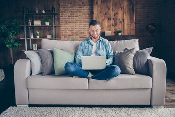 Photo of handsome homey guy relaxing sitting comfy couch legs crossed browsing notebook freelancer remote work staying home good mood quarantine time living room indoors