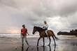 © Asia Pics - Asia, Indonesia, Bali, young Caucasian man with a beautiful young caucasian woman sitting on a horse, on a beach at sunset, with typical balinese rock formation situated in the sea