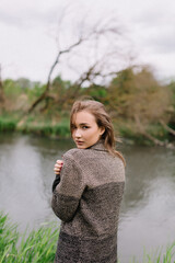 Wall Mural - Girl model portrait near the river with hair. Pensive look. Beautiful eyes. Stylish clothes on the nature. Trees and plants.