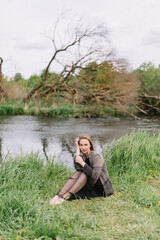 Wall Mural - Stylish model girl in clothes on the grass near the small river reeds trees