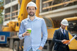 © zinkevych - Foreman holding coffee cup, smiling, building supervisor standing behind him with tablet