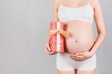 Cropped image of pregnant woman in white underwear holding a gift box and touching her belly at blue background. Expecting a baby girl. Copy space