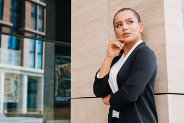 Elegant stylish lady is standing in a black formal suit leaning on the wall of a business center. girl closed her eyes in pleasure