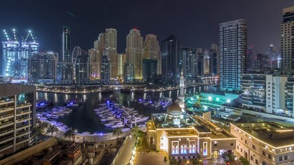 Wall Mural - Yachts in Dubai Marina flanked by the Al Rahim Mosque and residential towers and skyscrapers aerial timelapse during all night with lights switching off. Modern high rise skyline with boats and wooden