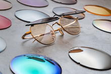 Assortment Of Different Multicolored Lenses For Eyewear, Fashion Trendy Sunglasses With Changeable Lenses Lying On Table In Professional Optical Shop. Optician Technician And Eyesight Concept 