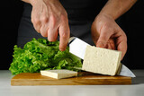 Fototapeta Kosmos - Chef cuts tofu cheese on a wooden board. High quality photo