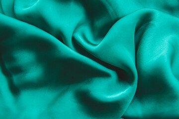Close up picture of silk fabric with wavy holds in green color for fashion photography to show fabric shade. Textured background of soft satin for fashion clothes. Emerald green color shade.