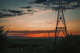 Fototapeta  - Power line structures in the field against the red sun