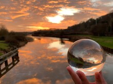 Red Clouds In The Sky Reflected In Both The River And In A Lens Ball Held Close To The Camera