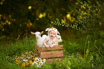 Portrait of a cute happy boy of 10-12 months in a gnome costume with white goats in spring on nature in a village with greenery and flowers.