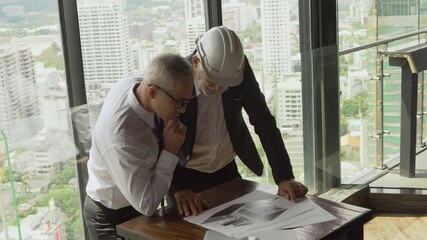 Wall Mural - mature architect  talking with senior business manager or Project owner with plan to construction on tall building cityscape background