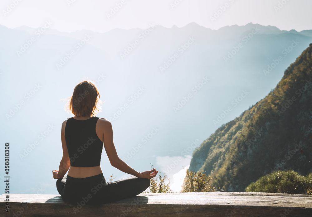 Young woman is meditating in mountains. - obrazy, fototapety, plakaty 