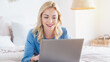 © InsideCreativeHouse - Portrait of smiling woman lying down on bed and using her laptop.