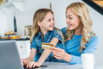 Young caucasian woman online shopping using credit card with her daughter at home