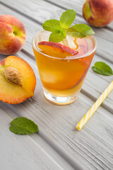 Wall Mural - Cold tea with peaches in the glass on the grey wooden background. Location vertical.