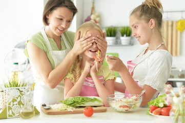 Wall Mural - Cute girls with mother preparing delicious fresh salad in kitchen